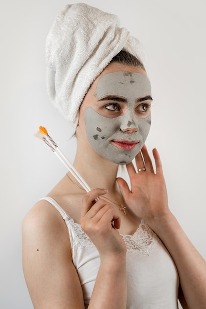 mulher caucasiana aplicando máscara de barro com escova em seu rosto cuidado da pele hidratante conceito de saúde