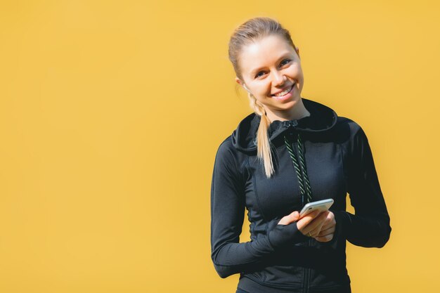 Mulher caucasiana atraente em terno esporte com fones de ouvido sem fio, usando o telefone para ouvir música em laranja