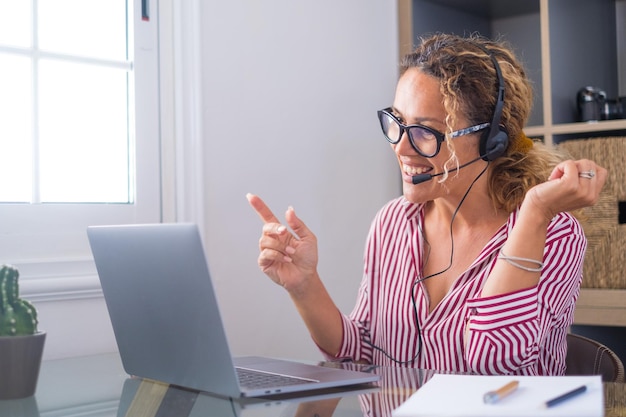 Mulher caucasiana atraente sentada na sala de escritório em casa usando fone de ouvido participa de webinar educacional usando laptop Evento de chamada de vídeo com clientes ou bate-papo pessoal com amigo remotamente conceptxA