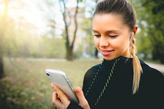 Mulher caucasiana atraente usando seu telefone, fone de ouvido sem fio enquanto estiver correndo no parque