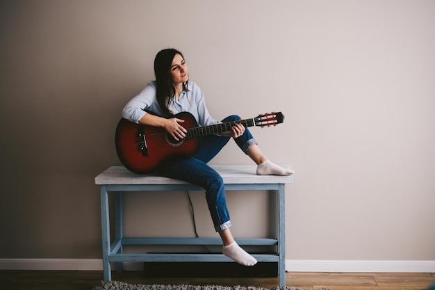 Mulher caucasiana bonita com cabelos pretos longos toca guitarra no interior no escandinavo