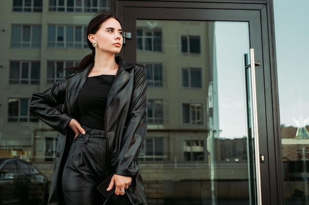 Foto mulher caucasiana bonita morena vestida de couro com bolsa de ombro andando do lado de fora da rua