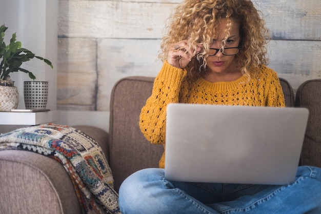 Mulher caucasiana concentrada em casa usando um notebook e tendo problemas de visão com óculos e dispositivo de tela