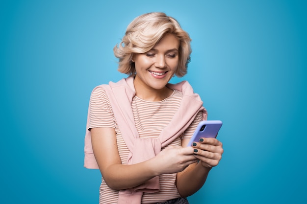 Mulher caucasiana conversando no celular e sorrindo alegremente na parede azul do estúdio
