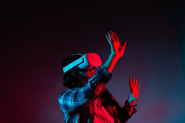 Mulher caucasiana de 35-40 anos em óculos de vr, usando fone de ouvido de realidade virtual, tentando tocar em algo com a mão na luz de néon.