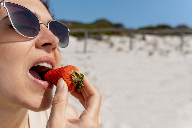 Mulher caucasiana de close-up mordendo um morango. garota na praia de óculos escuros.