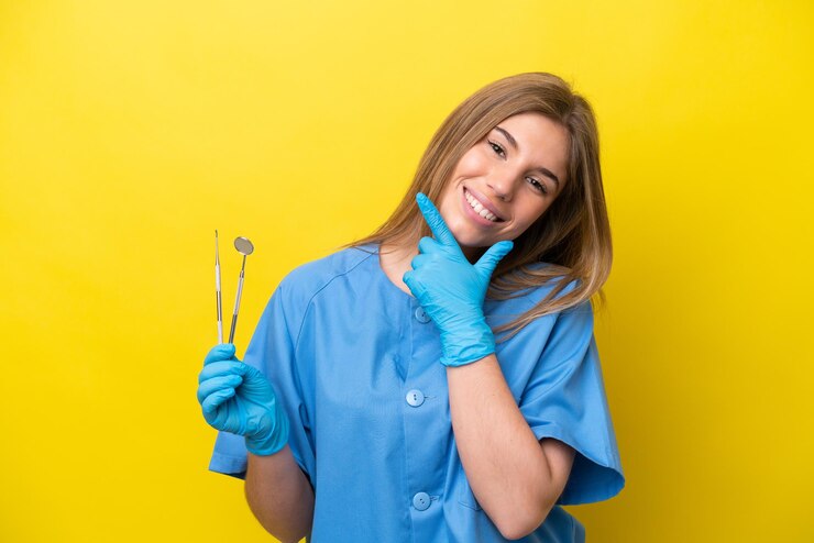 Foto mulher caucasiana de dentista segurando ferramentas isoladas em fundo amarelo feliz e sorridente