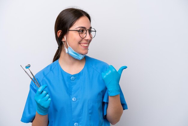 Foto mulher caucasiana de dentista segurando ferramentas isoladas no fundo branco apontando para o lado para apresentar um produto