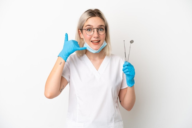 Foto mulher caucasiana de dentista segurando ferramentas isoladas no fundo branco, fazendo gesto de telefone. ligue-me de volta sinal