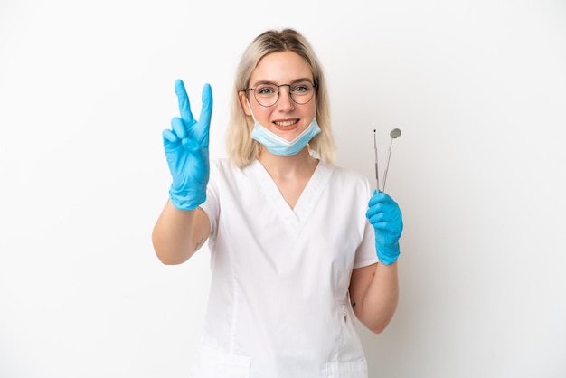 Mulher caucasiana de dentista segurando ferramentas isoladas no fundo branco, sorrindo e mostrando o sinal da vitória