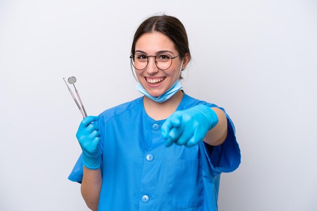 Mulher caucasiana de dentista segurando ferramentas isoladas no fundo branco surpresa e apontando para a frente