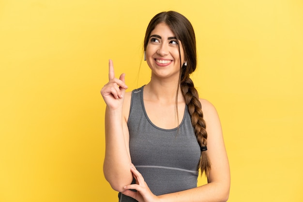 Mulher caucasiana de esportes isolada em um fundo amarelo apontando para uma ótima ideia