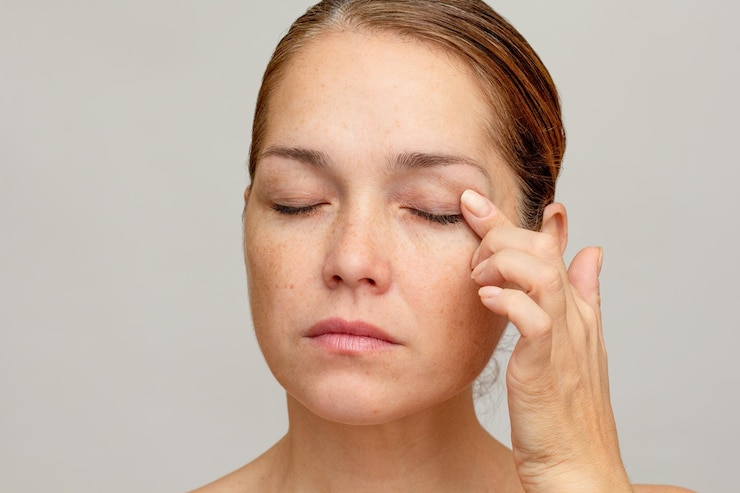 Foto mulher caucasiana de meia-idade com os olhos fechados segurando o dedo na pálpebra para mostrar os olhos envelhecendo