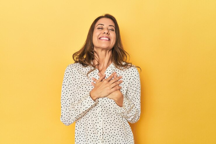 Foto mulher caucasiana de meia idade em amarelo rindo mantendo as mãos no coração conceito de felicidade