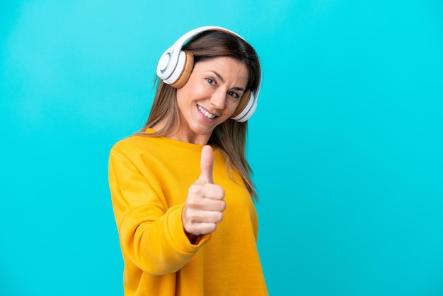 Mulher caucasiana de meia-idade isolada em fundo azul ouvindo música e com o polegar para cima