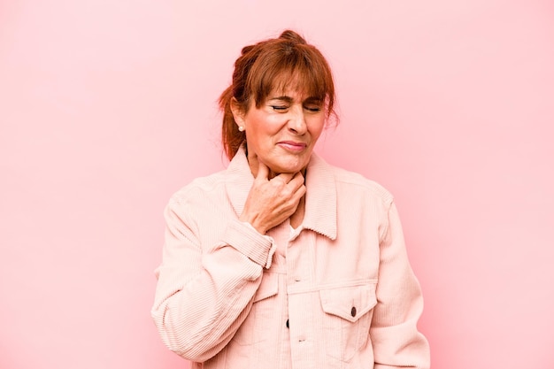 Mulher caucasiana de meia idade isolada em fundo rosa sofre dor na garganta devido a um vírus ou infecção