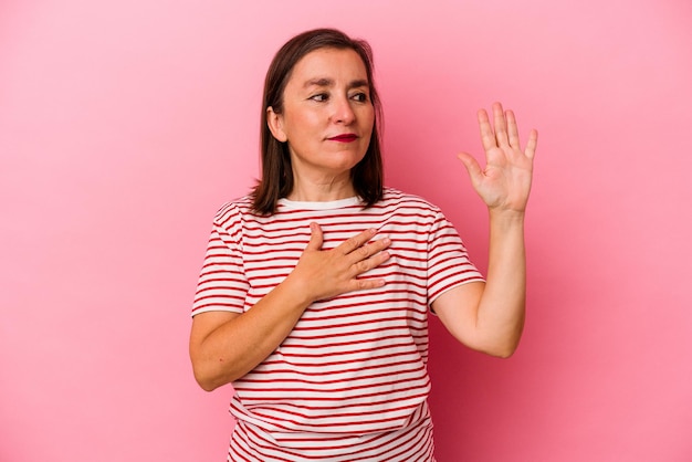 Mulher caucasiana de meia-idade isolada no fundo rosa, fazendo um juramento, colocando a mão no peito.