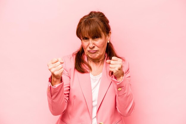 Mulher caucasiana de meia-idade isolada no fundo rosa, mostrando o punho para a expressão facial agressiva da câmera