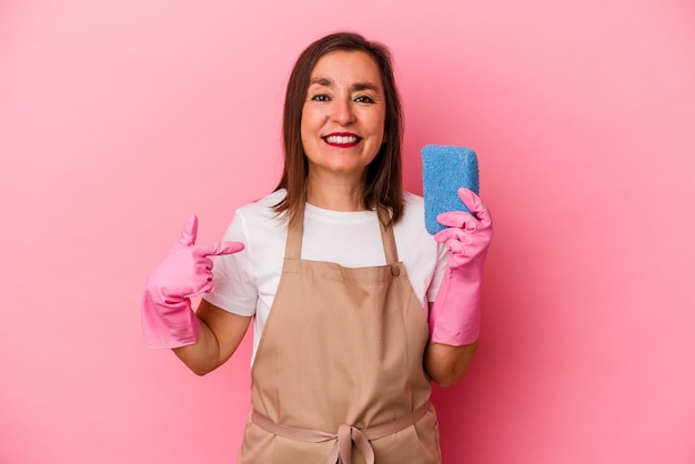 Mulher caucasiana de meia idade limpando a casa isolada na pessoa de fundo rosa apontando com a mão para um espaço de cópia de camisa, orgulhoso e confiante