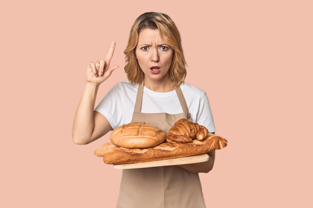 Foto mulher caucasiana de meia-idade padeira com bandeja de pão tendo uma ideia conceito de inspiração