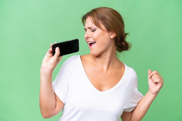 Mulher caucasiana de meia idade sobre fundo isolado usando telefone celular e cantando