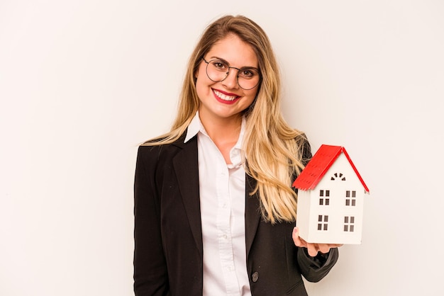 Mulher caucasiana de negócios jovem segurando uma casa de brinquedos isolada em fundo branco feliz sorrindo e alegre