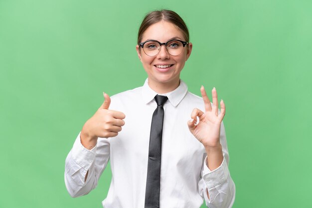 Mulher caucasiana de negócios jovem sobre fundo isolado mostrando sinal ok e polegar para cima gesto