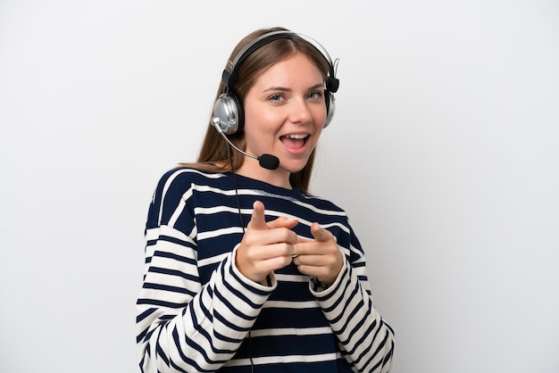 Mulher caucasiana de telemarketing trabalhando com um fone de ouvido isolado no fundo branco, apontando para a frente e sorrindo