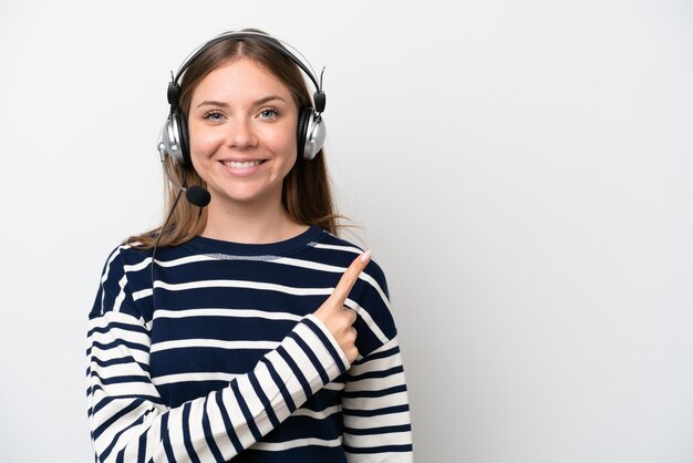 Mulher caucasiana de telemarketing trabalhando com um fone de ouvido isolado no fundo branco, apontando para o lado para apresentar um produto