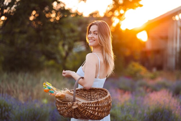 Mulher caucasiana de vestido branco caminha no prado de lavanda na noite de verão na hora dourada