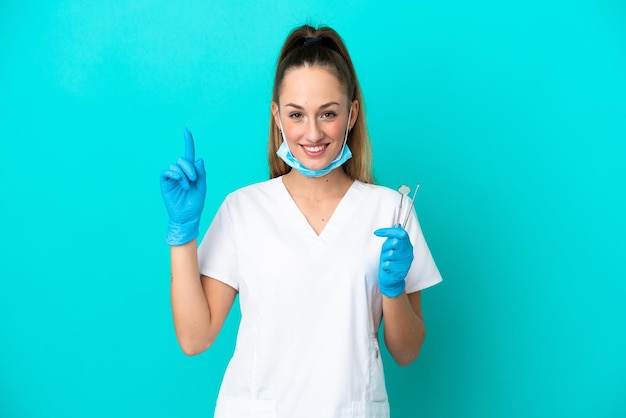 Mulher caucasiana dentista segurando ferramentas isoladas em fundo azul apontando uma ótima ideia