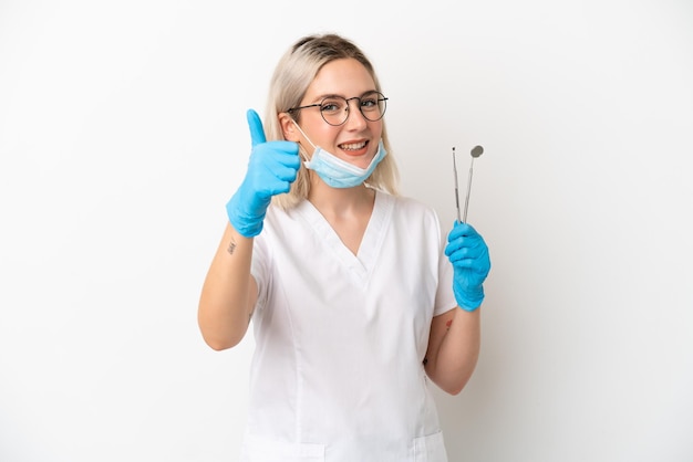 Mulher caucasiana dentista segurando ferramentas isoladas em fundo branco com polegares para cima porque algo bom aconteceu