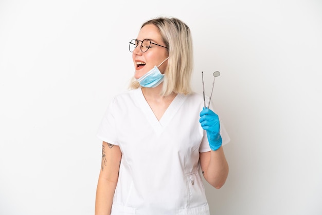 Mulher caucasiana dentista segurando ferramentas isoladas no fundo branco rindo na posição lateral