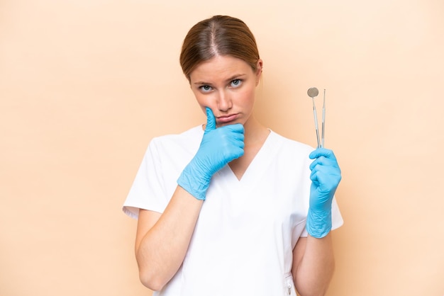 Mulher caucasiana dentista segurando ferramentas isoladas no pensamento de fundo bege