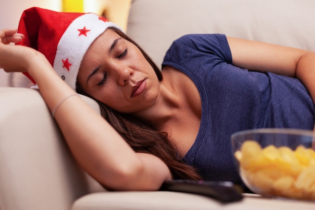 Mulher caucasiana dormindo no sofá depois de assistir a um filme de entretenimento de natal