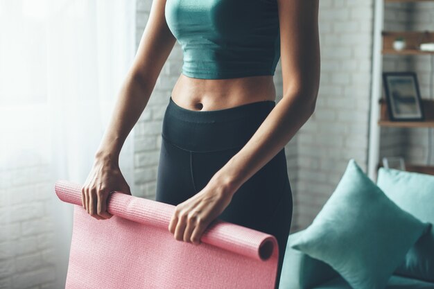 Mulher caucasiana em forma usando roupas esportivas enquanto pega o tapete de ioga