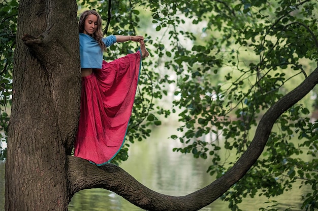 Mulher caucasiana em pé no equilíbrio de ioga pose de utthita hasta padangusthasana ela segura o tronco da árvore