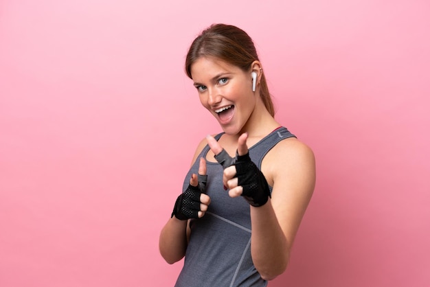 Mulher caucasiana esportiva jovem isolada em fundo rosa, apontando para a frente e sorrindo