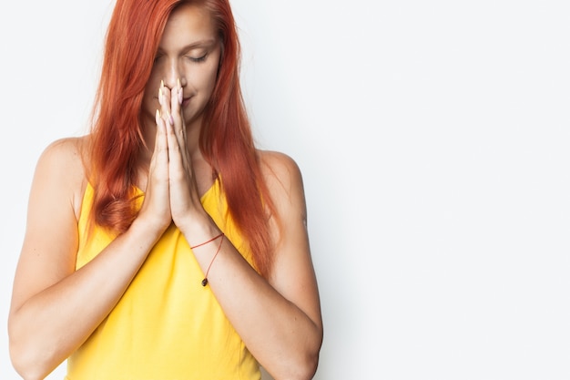 Mulher caucasiana está orando na parede de um estúdio branco com as palmas das mãos juntas e fechando os olhos