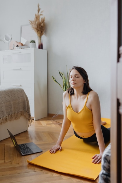 Mulher caucasiana europeia faz ioga e meditação em sua casa para acalmar ioga em um tapete amarelo