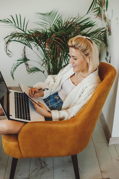 Mulher caucasiana fazendo cursos on-line sentada em uma poltrona com laptop estudando on-line