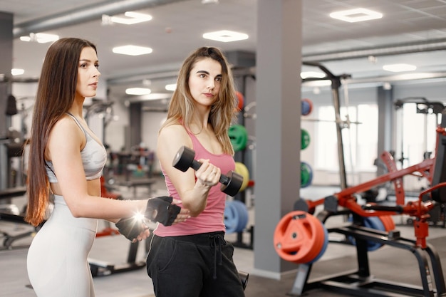 Mulher caucasiana fazendo exercícios na academia com personal trainer feminino