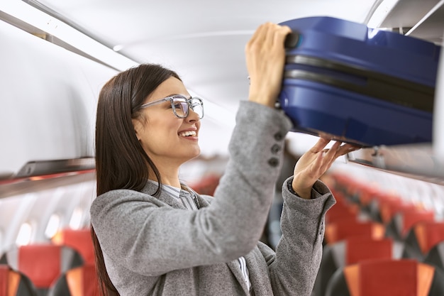 Mulher caucasiana feliz com bagagem no salão do avião