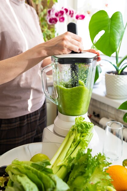 Mulher caucasiana feliz e alegre com uma camiseta na cozinha fazendo um smoothie verde