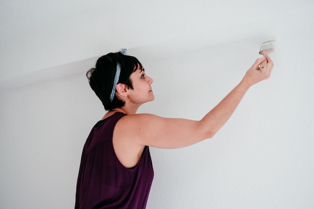 Mulher caucasiana feliz pintando as paredes do quarto com cor branca fazê-lo você mesmo e novo conceito de casa