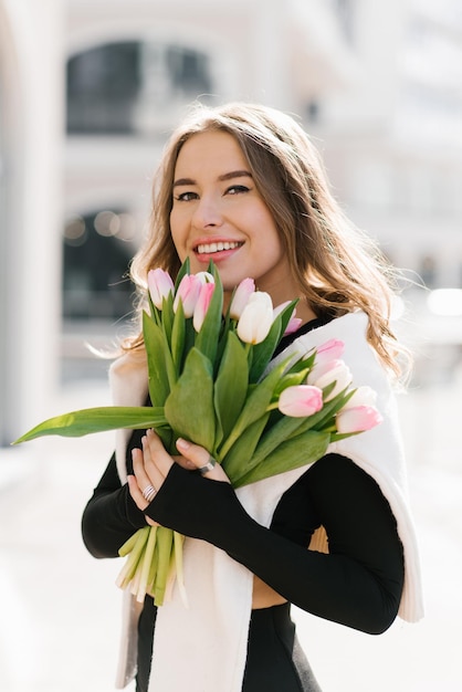 Mulher caucasiana feliz segura um buquê de flores de primavera em suas mãos enquanto caminha pela cidade