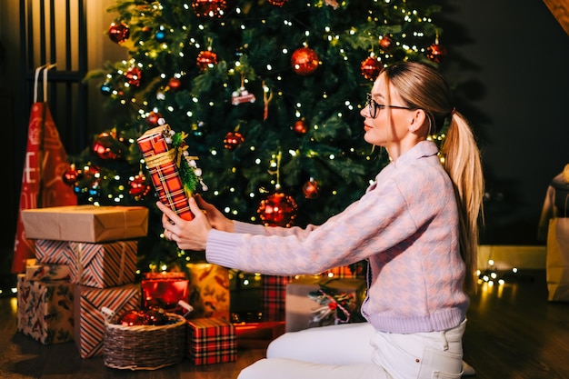 Mulher caucasiana feliz segurando um grande presente de Natal perto da árvore de Natal.