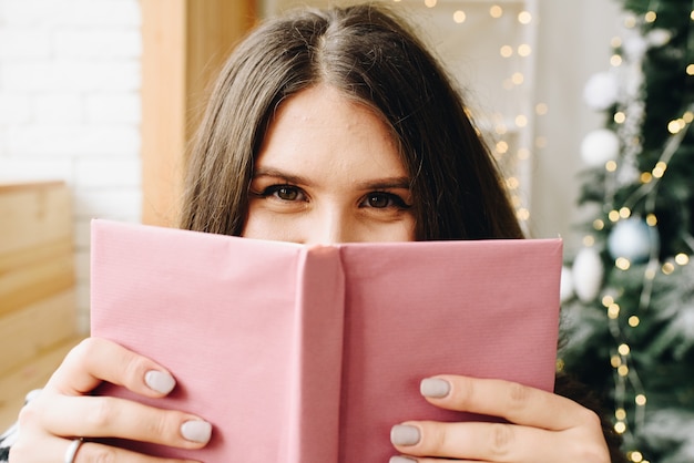 Mulher caucasiana feliz segurando um livro roxo perto da árvore de Natal decorada