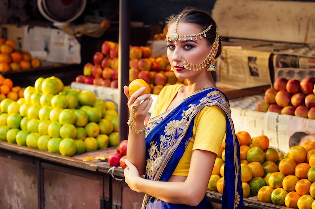 Mulher caucasiana indiana em dress.hindu modelo dourado kundan jóias conjunto brincos bindi e piercing no nariz nath escolhendo frutas comprador em uma loja de frutas de supermercado.exotic venda Kerala Goa