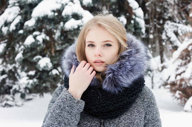 Mulher caucasiana inspirada em lenço de lã, desviar o olhar com um sorriso enquanto posava na manhã de inverno. Retrato do close-up feminino fascinante em pé no pátio nevado. Tempo frio e ensolarado. Conceito de inverno da mulher.